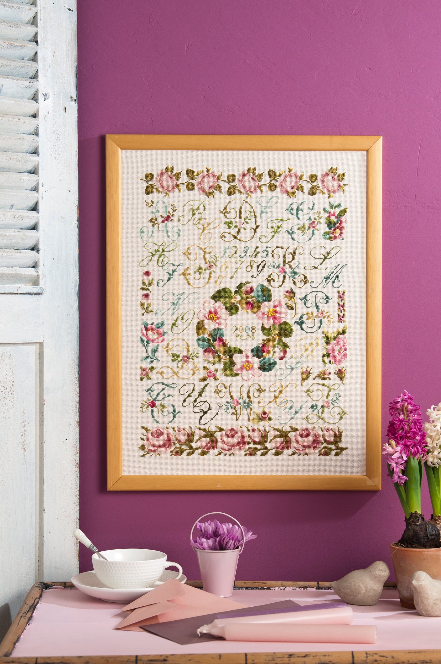 Abécédaire aux lettres anglaises brodé sur lin clair : arabesques, couronne fleurie et roses anciennes en rose poudré et vert tendre. Sampler romantique, 32,7 × 43,6 cm.