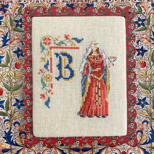 Grille point de croix : alphabet médiéval, damoiselles et motifs floraux. 52×52 pts, lin 11 fils/cm ou Aïda 5,5 pts/cm. 6 pages couleur, réf. DMC.