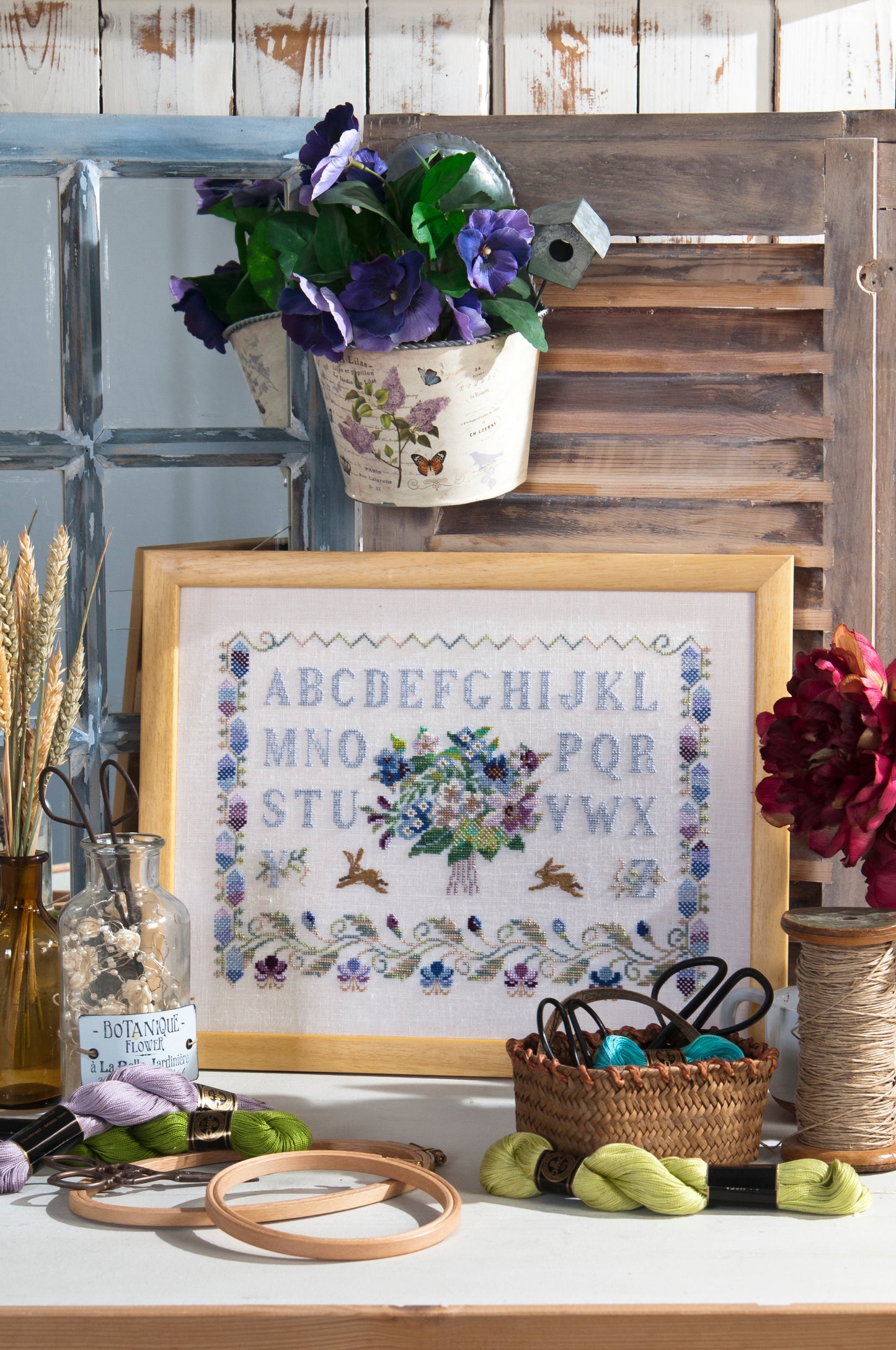 Abécédaire printanier brodé sur lin clair : lapins, fleurs et frises en bleu pervenche et rose poudré. Sampler romantique au point de croix, 32,7 × 23,6 cm.