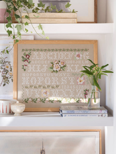Abécédaire printanier brodé sur lin naturel clair : lettres anciennes, roses et frises végétales en rose tendre et vert sauge. Sampler romantique, 40 × 32,7 cm.