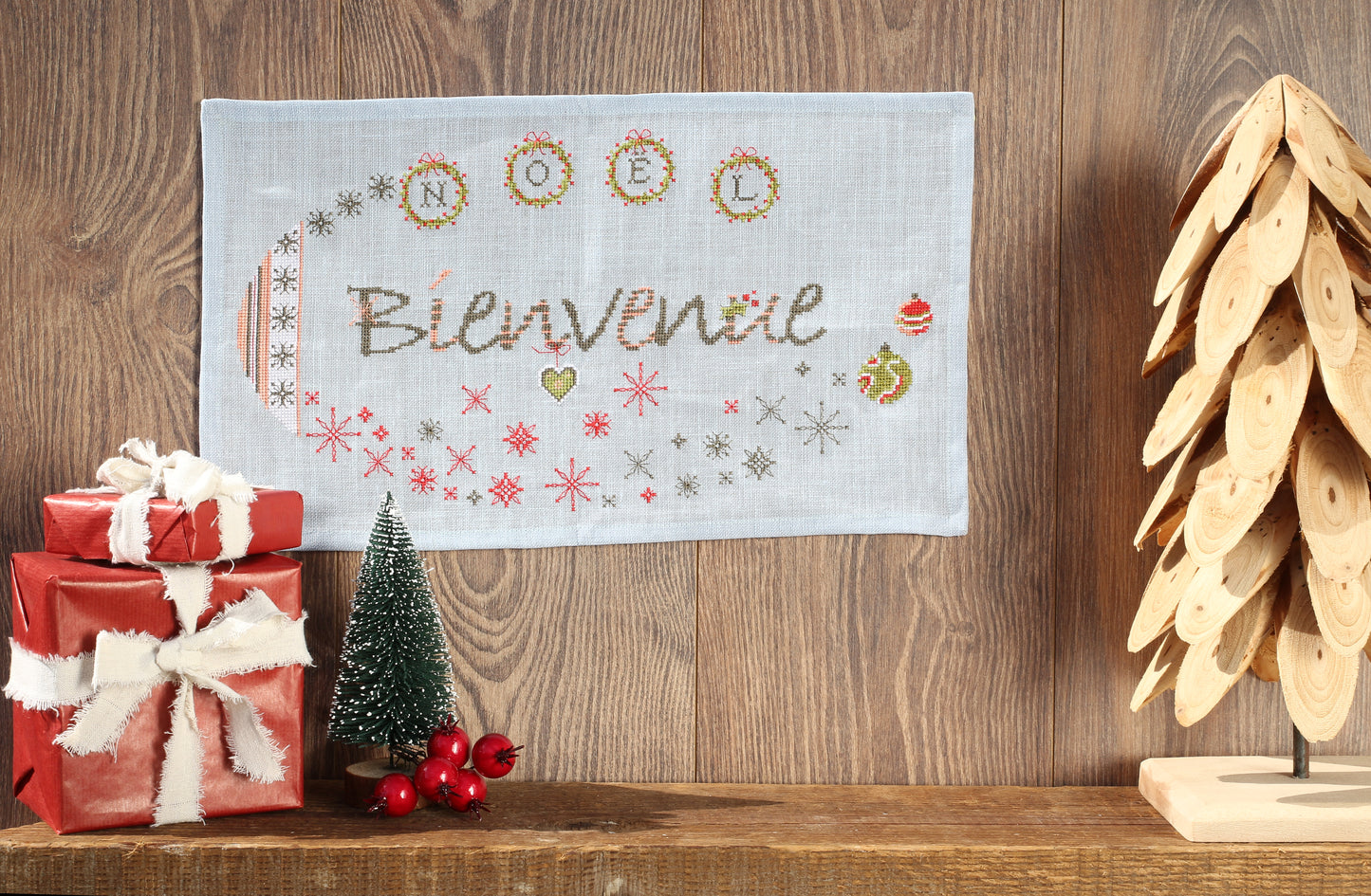 Grand panneau de Noël brodé sur lin bleu jeans 12 fils/cm : lettres et motifs festifs en rouge, blanc et vert. Esprit chic et contemporain, 39,8 × 21,8 cm.