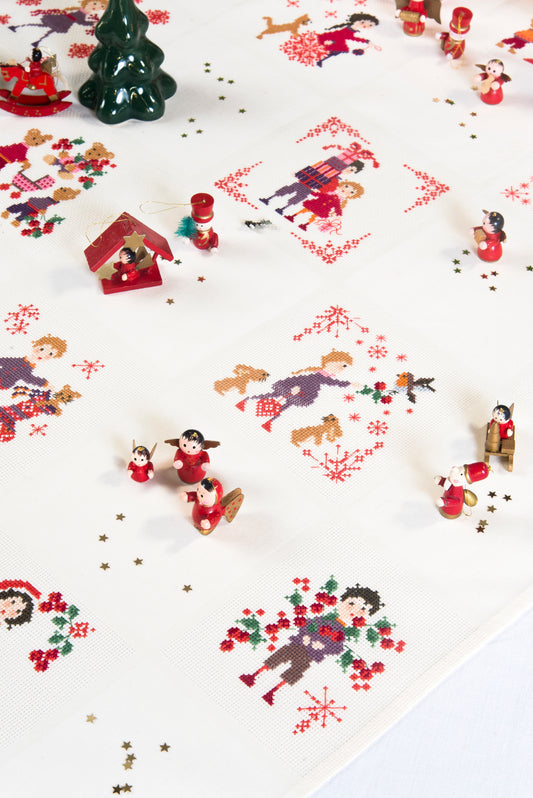 Grille point de croix : nappe de Noël avec personnages, sapins et flocons. 56×56 pts, Aïda 5,5 pts/cm ou lin 11 fils/cm. 10 pages couleur, réf. DMC.