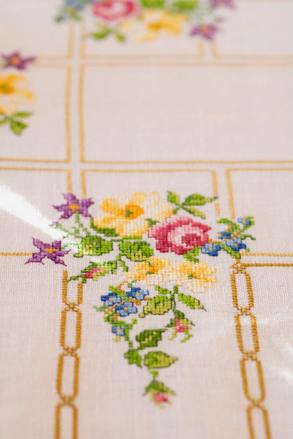 Grille de broderie point de croix « Nappes fleuries » : motifs fleuris et chaînes dorées à broder sur nappe lin blanc 11 fils. DMC, 8 pages.