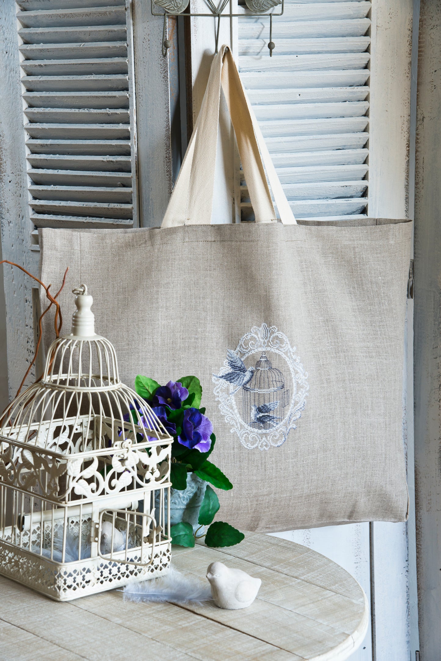 Scène romantique brodée sur sac cabas en lin naturel : cage ancienne et oiseaux amoureux en camaïeu gris bleuté. Motif 18,2 × 21,8 cm, esprit gravure vintage.