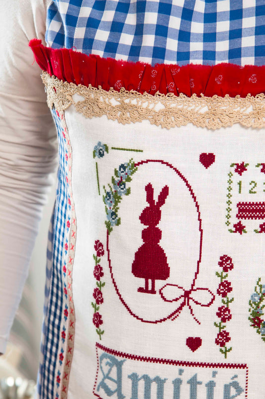 Grille de point de croix Tablier Porte Bonheur par Lili Violette : Mademoiselle lapin, fleurs et lettres. 292 x 180 points. Références DMC sur 6 pages.
