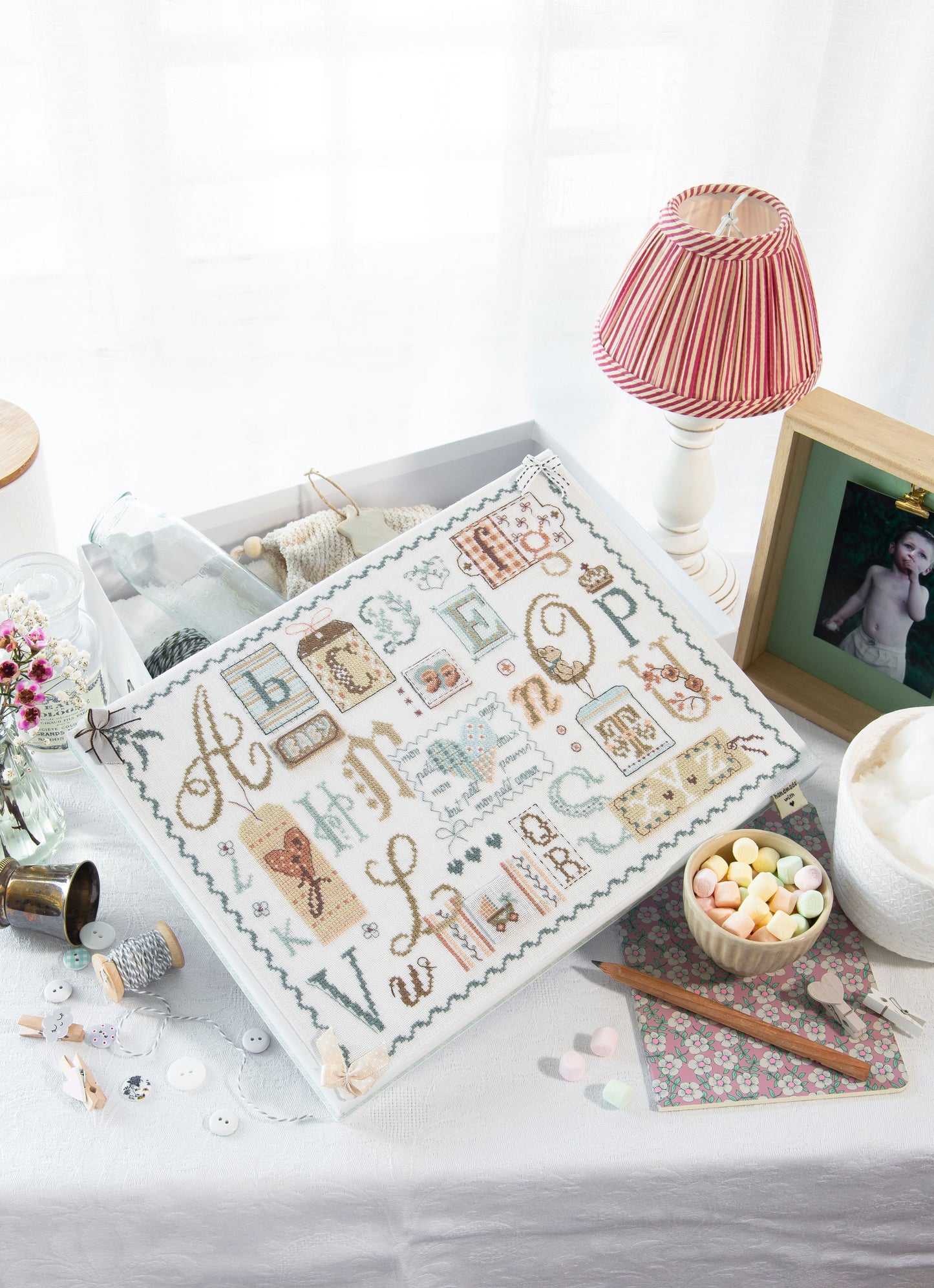 Grille point de croix – Abécédaire en lin brodé pour bébé : bébé endormi entouré de lettres délicates sur toile de lin blanc DMC, idéal comme cadeau de naissance – Véronique Enginger & Création Point de Croix