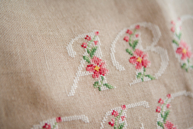 Abécédaire floral brodé sur lin naturel : lettres majuscules fleuries en rose ancien et vert feuillage. Motif romantique pour coussin, 27,3 × 27,3 cm.