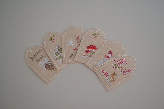 Brodez six étiquettes de Noël au point de croix pour personnaliser vos cadeaux : mots doux et motifs d’hiver. 41 × 70 points sur lin Zweigart 16 fils/cm.