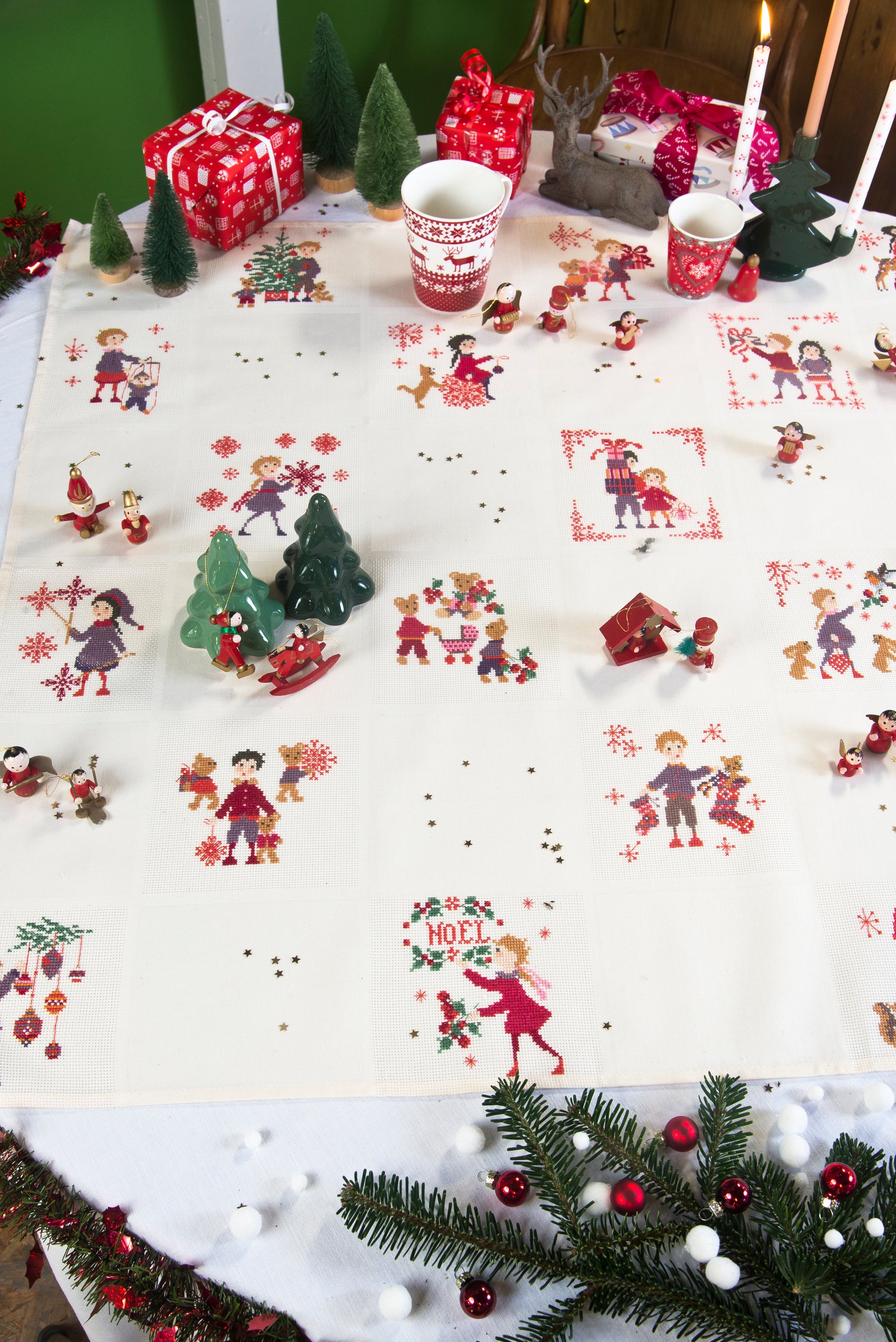 Grille point de croix : nappe de Noël avec personnages, sapins et flocons. 56×56 pts, Aïda 5,5 pts/cm ou lin 11 fils/cm. 10 pages couleur, réf. DMC.