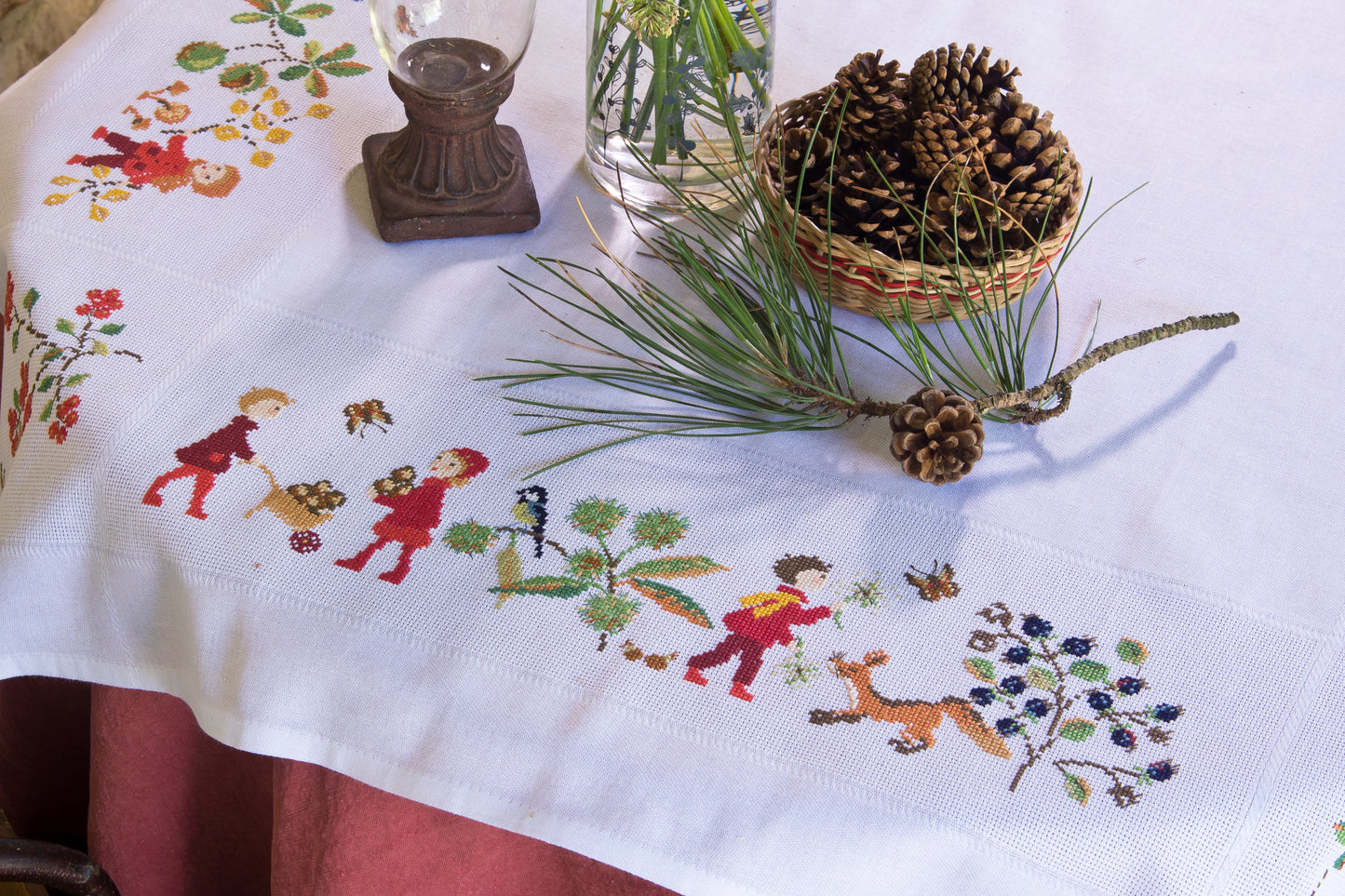 Grille point de croix : nappe d’automne à broder sur toile blanche 5,5 pts. Feuilles, fruits et personnages. 12 pages DMC. Linge de table automnal.