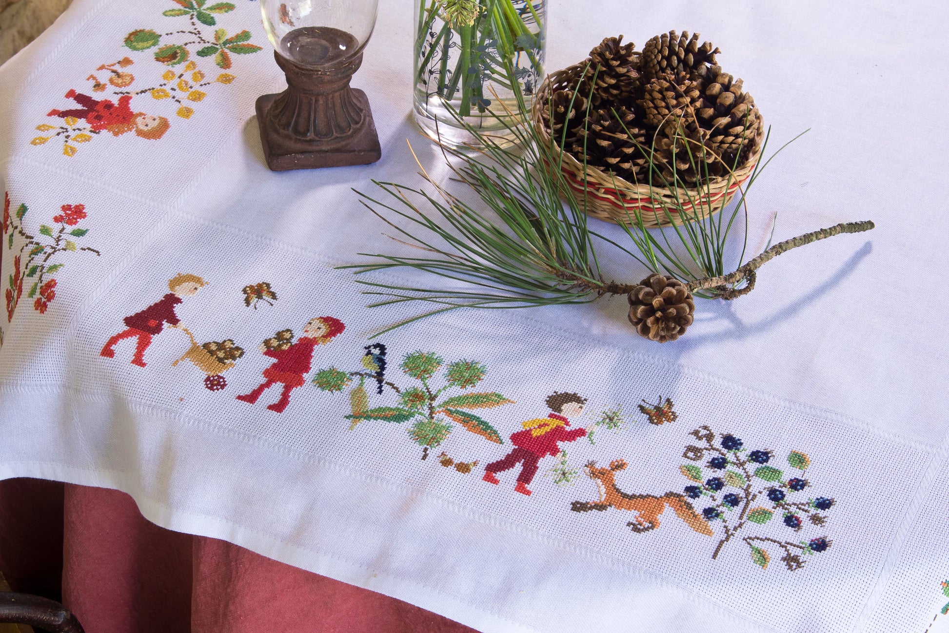 Grille point de croix : nappe d’automne à broder sur toile blanche 5,5 pts. Feuilles, fruits et personnages. 12 pages DMC. Linge de table automnal.