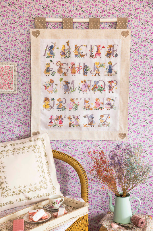 Grille point de croix : abécédaire Rose au chapeau, fleurs et pastel. 256×299 pts, Aïda 5,5 pts/cm ou lin 11 fils/cm. Réf. DMC, 8 pages.