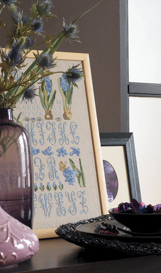 Grandes lettres ornées et jacinthes bleuées brodées sur lin naturel. Abécédaire floral romantique au point de croix, 21,8 × 32,7 cm, esprit herbier ancien.