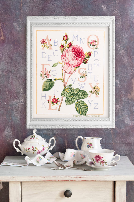 Grille point de croix – Abécédaire rose : grande rose épanouie inspirée de Redouté, boutons et feuillages finement dessinés entourant un alphabet élégant sur toile de lin – DMC & Création Point de Croix
