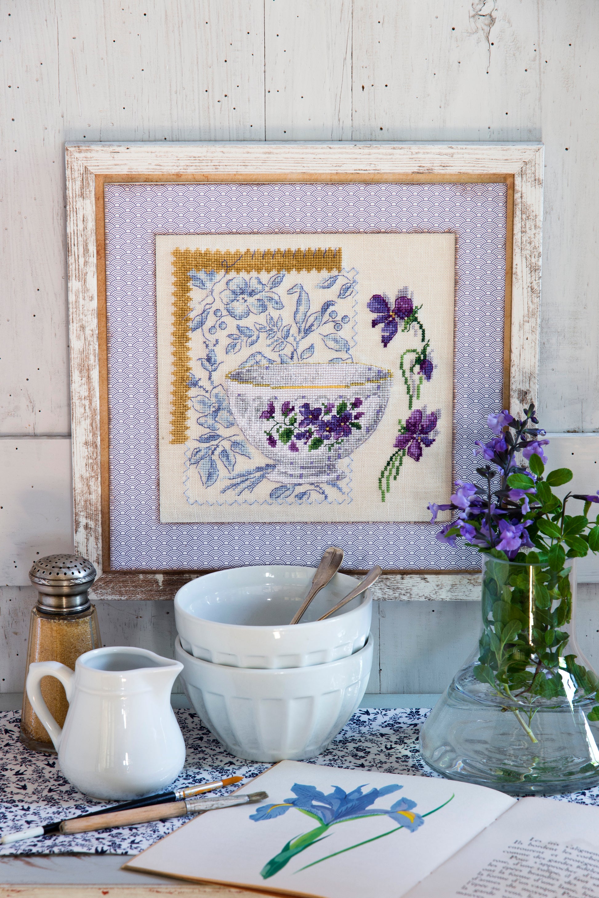 Grille point de croix – Bol violettes : bol en porcelaine blanche orné de violettes mauves et violettes sur fond de tissu fleuri bleu, ambiance romantique et printanière – Création Point de Croix"