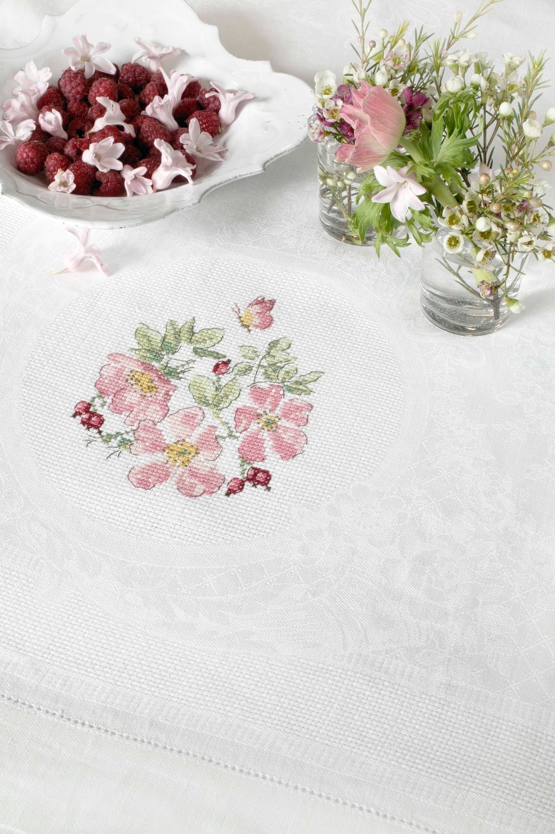 Grille broderie point de croix : nappe de fête avec couronne d'églantines. Imprimée en couleur sur 6 pages. Réf. DMC incluses.
