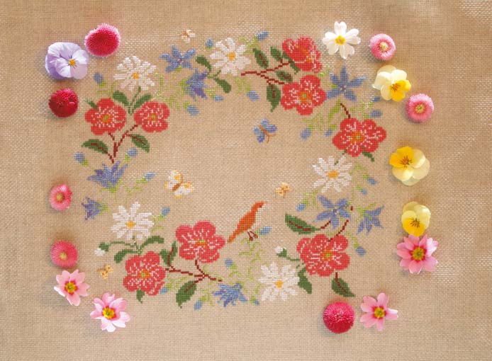 Grille broderie point de croix : couronne de fleurs printanières, motif 157×147 pts, 28,5×26,7 cm. Symboles + couleurs DMC, 6 pages.