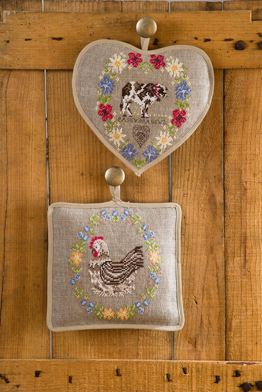 Grille point de croix – Couronnes champêtres : vache et poulette entourées de fleurs sauvages brodées sur housses de coussin en lin naturel, décoration bucolique et poétique – Marie-Anne Réthoret-Melin & Création Point de Croix