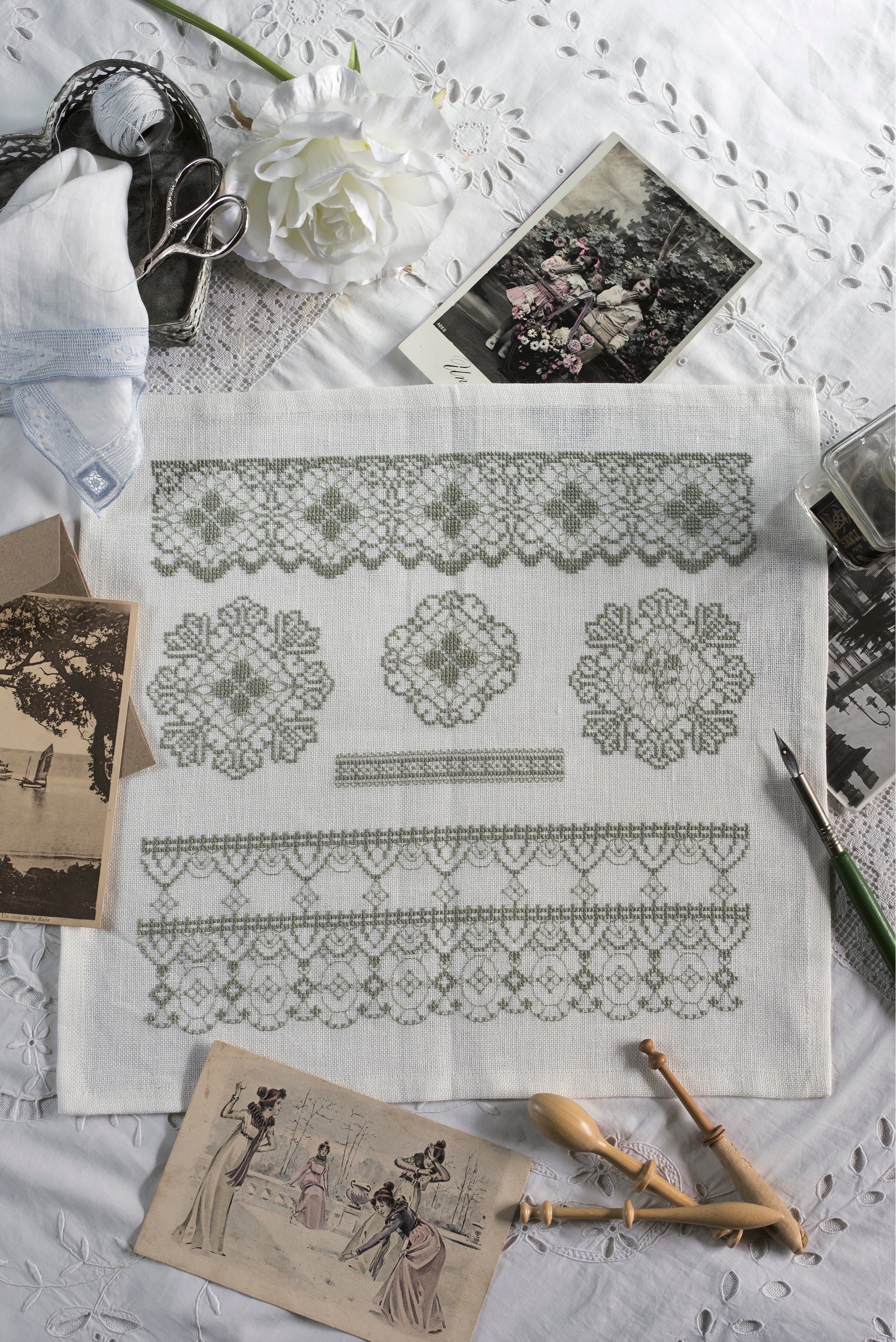 Frises et rosaces inspirées des dentelles anciennes brodées en vert sauge sur lin blanc 12 fils/cm. Motif raffiné pour linge de maison et coussins, 29 × 27,5 cm.