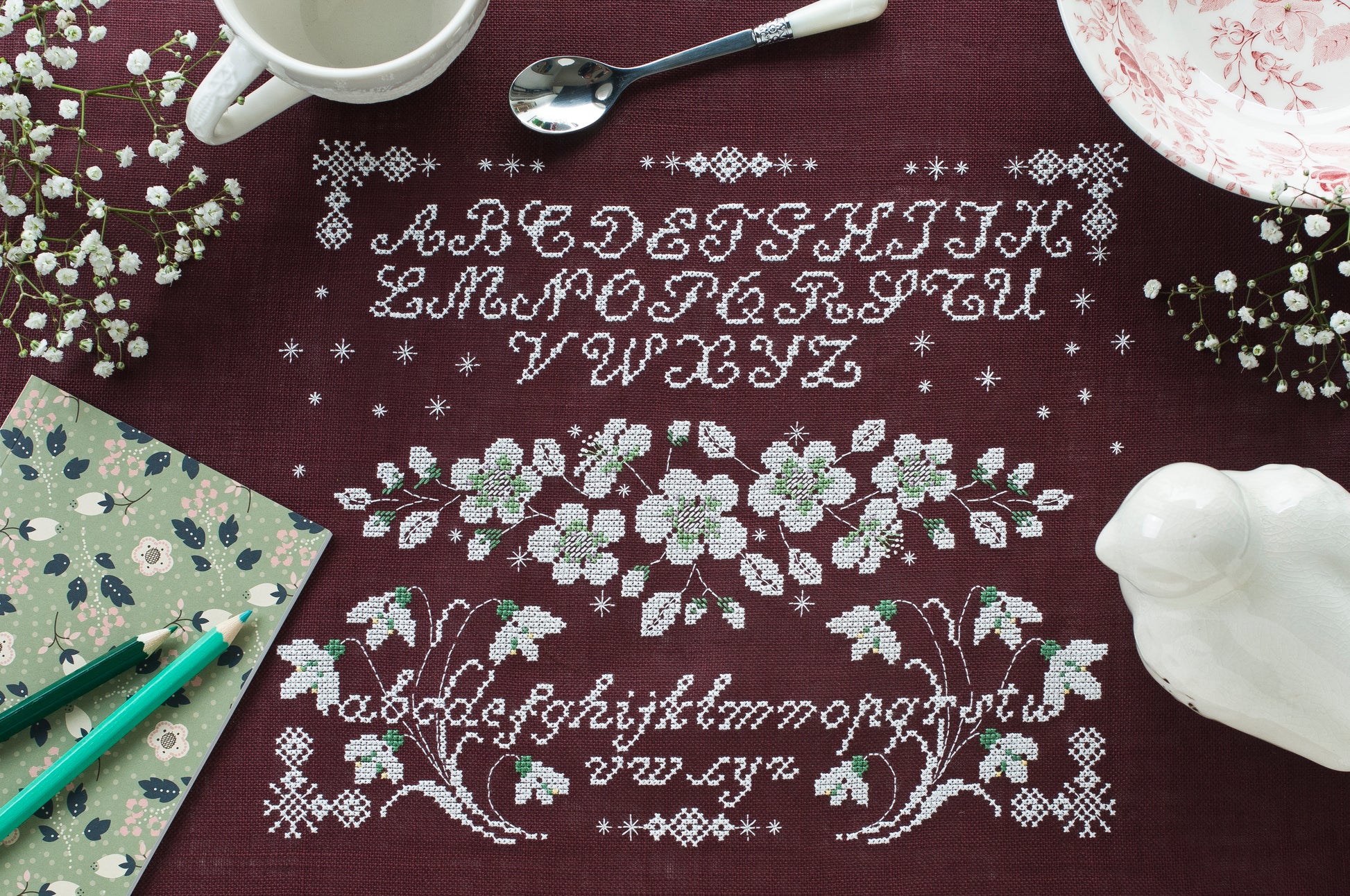 Sampler monochrome blanc sur toile lie de vin : hellébores, perce-neige et abécédaire ancien au point de croix. Esprit hiver romantique, 30 × 23,6 cm.
