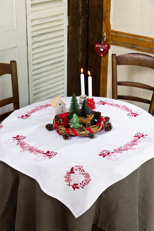 Grille point de croix – La magie de Noël sur votre table : nappe brodée avec motifs de houx, branches de sapin et cœurs entrelacés en rouge, vert et blanc, sur nappe à broder encadrée – Véronique Enginger & Création Point de Croix