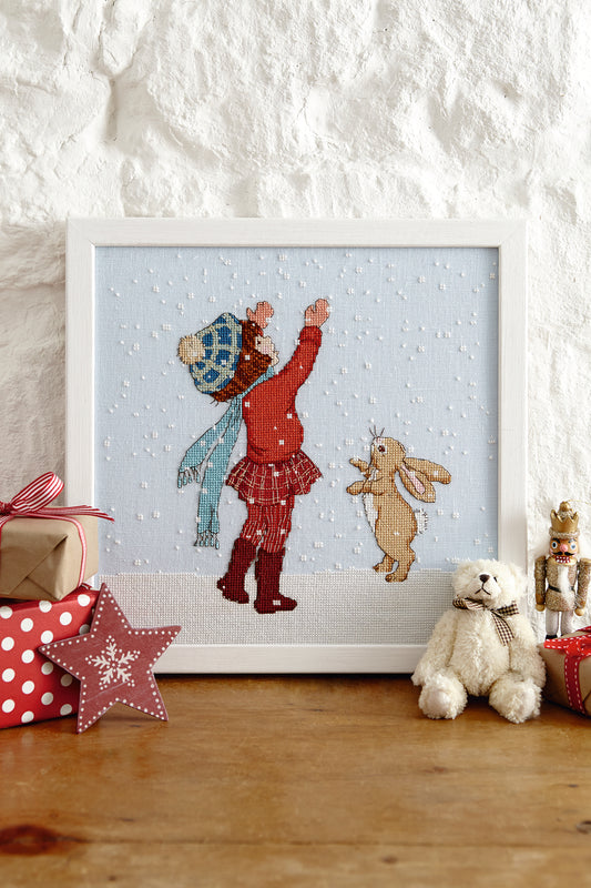 Grille de point de croix La Neige Tombe Bell & Boo – Belle emmitouflée dans son manteau rouge contemplant les premiers flocons avec Boo, brodé sur lin bleu clair 11 fils/cm, Création Point de Croix