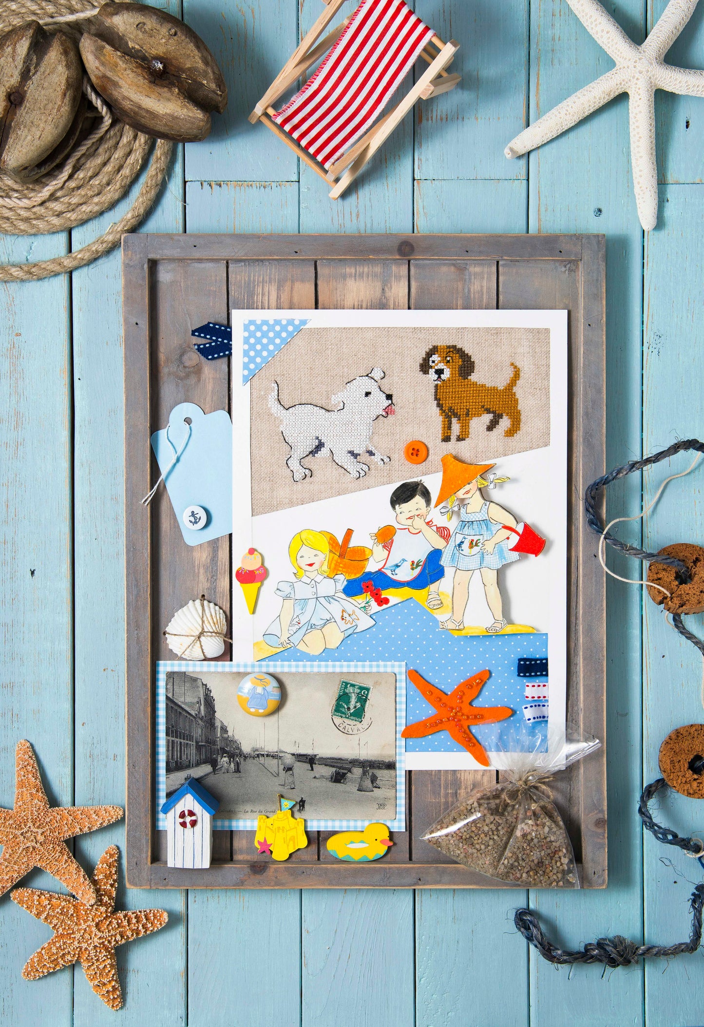 Grille point de croix – La plage : petits chiens espiègles et oiseaux marins brodés sur toile de lin DMC 842 11 fils/cm, mis en scène dans un cadre décoratif avec coquillages et carte postale ancienne – Création Point de Croix