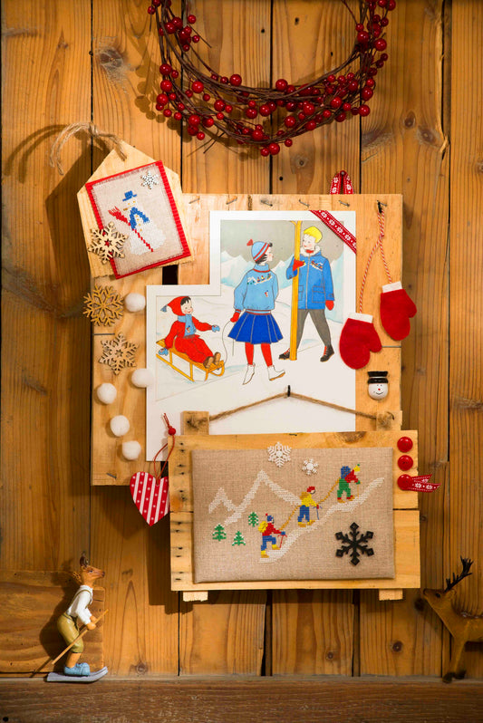Grille point de croix – Les sports d'hiver : bonhomme de neige, alpinistes en cordée et paysages enneigés brodés sur toile de lin DMC 842 11 fils/cm, mis en scène sur supports en bois décorés – Création Point de Croix