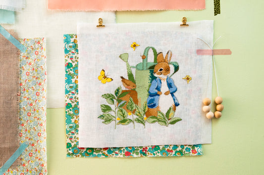 Grille point de croix Pierrot-Lapin caché derrière un arrosoir au potager – Motif broderie Beatrix Potter, Création Point de Croix