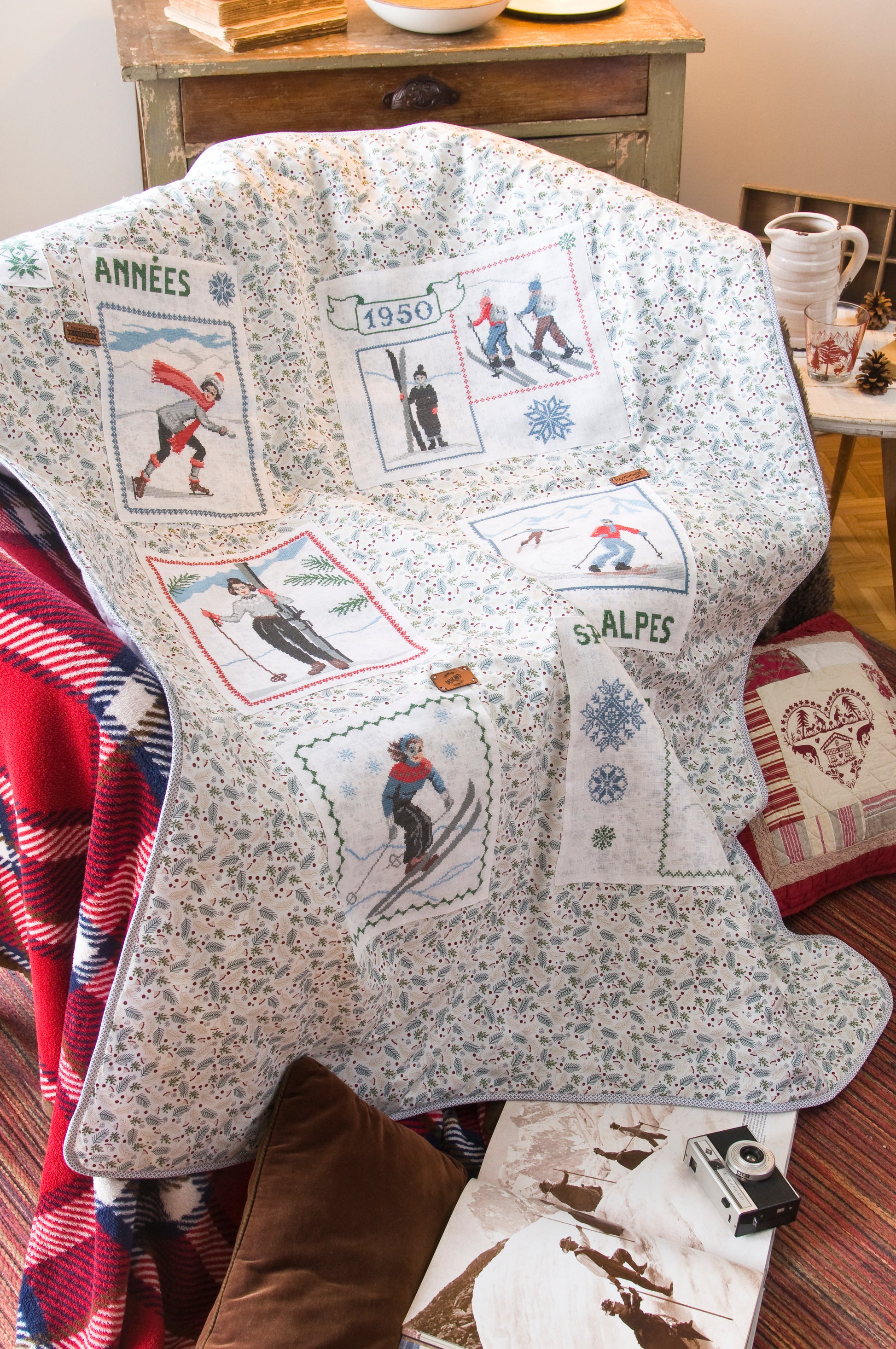 Grille de broderie point de croix : plaid skieurs années 30, silhouettes élégantes sur fond patchwork pastel. Imprimé couleur (Réf. DMC) sur 10 pages. Illustration Sylvie Teytaud.