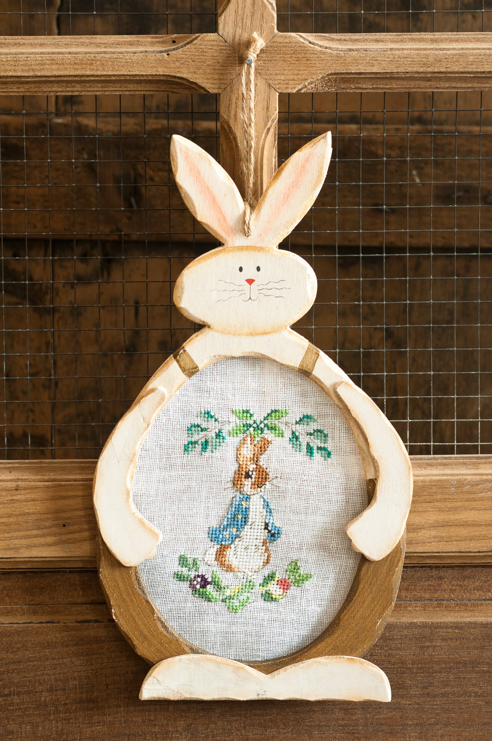 Grille point de croix – Suspension Pierrot-Lapin : Pierrot-Lapin dans le potager du paysan Poupon brodé sur toile de lin DMC B5200 11 fils/cm, présenté dans un cadre en bois découpé en forme de lapin, décoration chambre enfant – Création Point de Croix