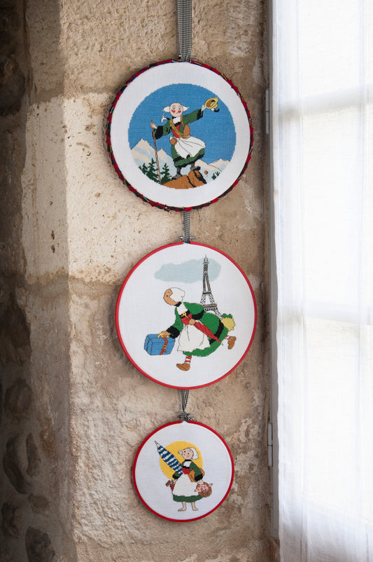 Grille broderie point de croix : tambours Bécassine en voyage (montagne, Paris, mer), 3 motifs 70×70 pts. Symboles + couleurs DMC, 6 pages.