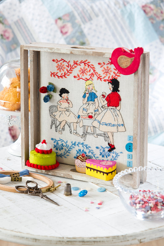 Grille point de croix – Tea Time : fillettes, frises de pâtisseries et théières brodées sur toile de lin ivoire DMC 3865 11 fils/cm, mis en scène dans des plateaux décoratifs avec éléments en feutrine – Création Point de Croix