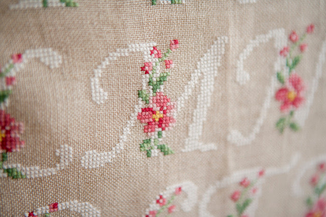 Abécédaire floral brodé sur lin naturel : lettres majuscules fleuries en rose ancien et vert feuillage. Motif romantique pour coussin, 27,3 × 27,3 cm.