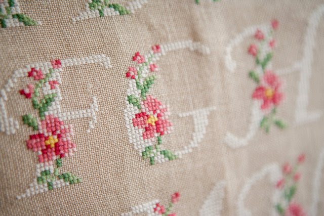 Abécédaire floral brodé sur lin naturel : lettres majuscules fleuries en rose ancien et vert feuillage. Motif romantique pour coussin, 27,3 × 27,3 cm.