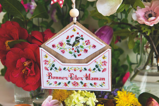 Grille point de croix : panneau enveloppe fleurie « Bonnes Fêtes Maman ». 79×70 pts, Aïda 7 pts/cm ou lin 14 fils/cm. 6 pages couleur, réf. DMC.