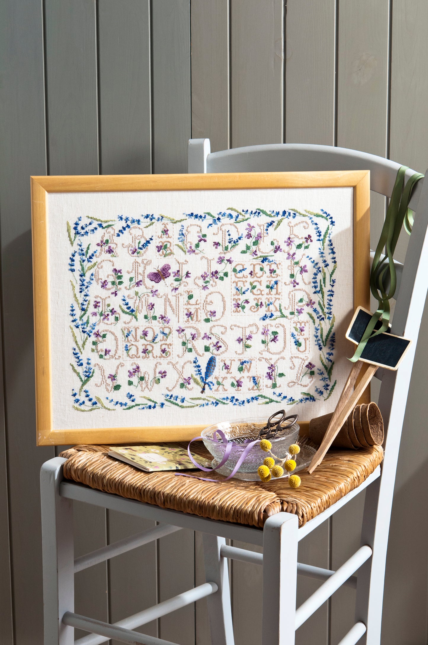 Sampler provençal brodé sur lin clair : lettres anciennes, lavande et papillon en bleu lavande et vert sauge. Esprit marquoir romantique, 32,7 × 23,6 cm.