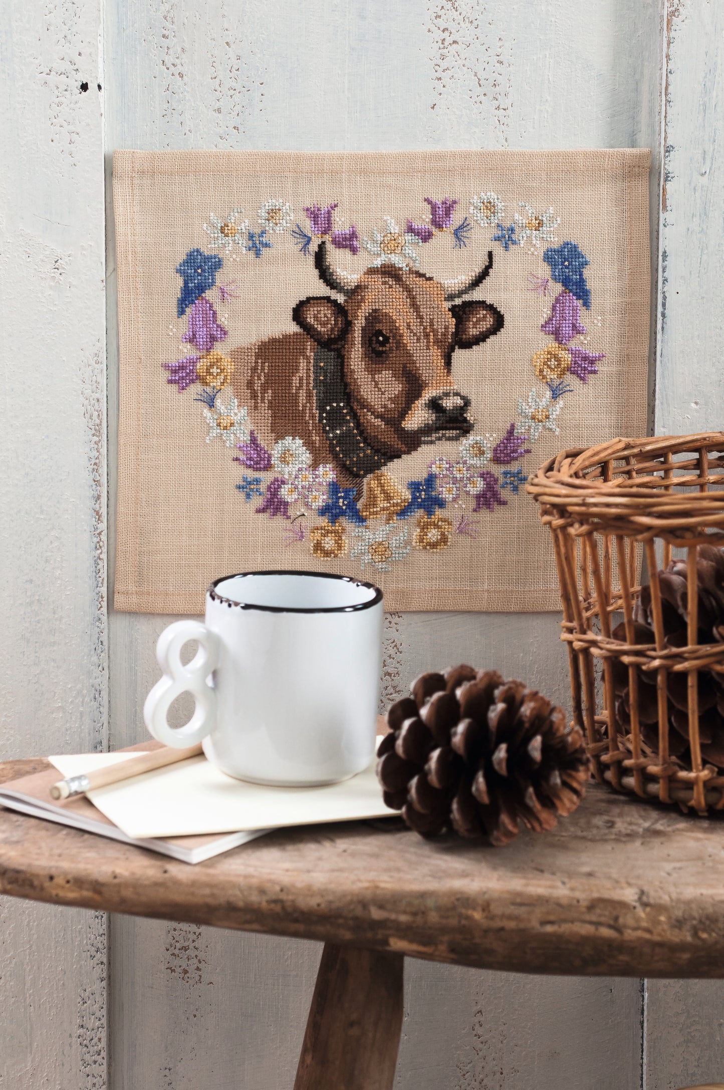 Grille point de croix – La vache Marguerite : vache emblématique entourée d'une couronne de fleurs champêtres brodée sur toile de lin sable 12 fils/cm, ambiance pâturage bucolique et décoration campagne – Monique Bonin & Création Point de Croix