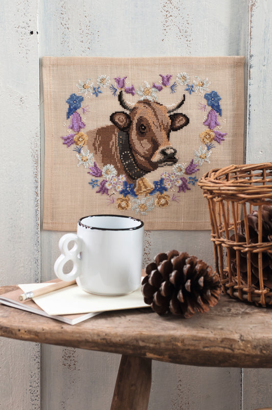 Grille point de croix – La vache Marguerite : vache emblématique entourée d'une couronne de fleurs champêtres brodée sur toile de lin sable 12 fils/cm, ambiance pâturage bucolique et décoration campagne – Monique Bonin & Création Point de Croix
