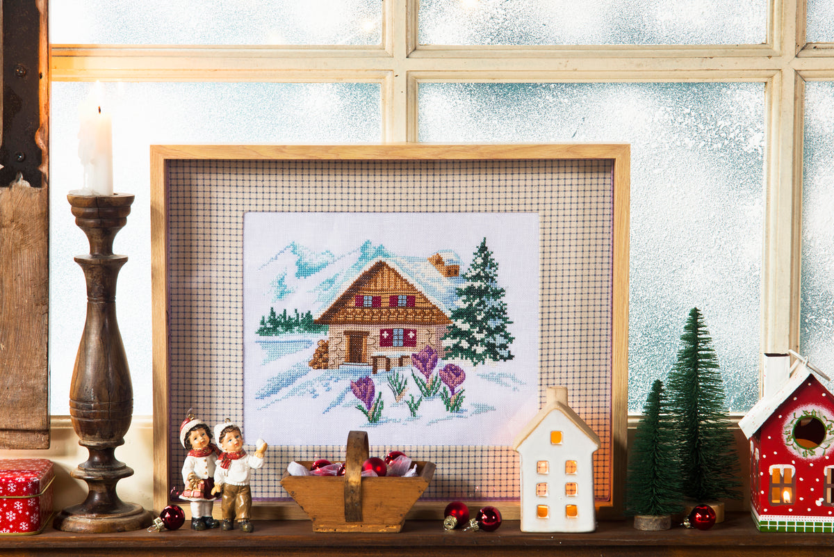 Brodez un chalet enneigé entouré de fleurs avec la grille Évasion montagnarde. Motif de 125 × 85 points, références de fils DMC.