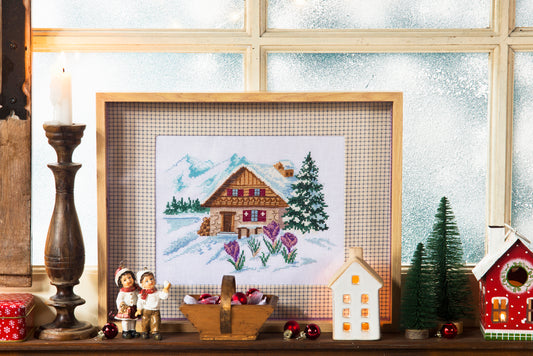 Brodez un chalet enneigé entouré de fleurs avec la grille Évasion montagnarde. Motif de 125 × 85 points, références de fils DMC.