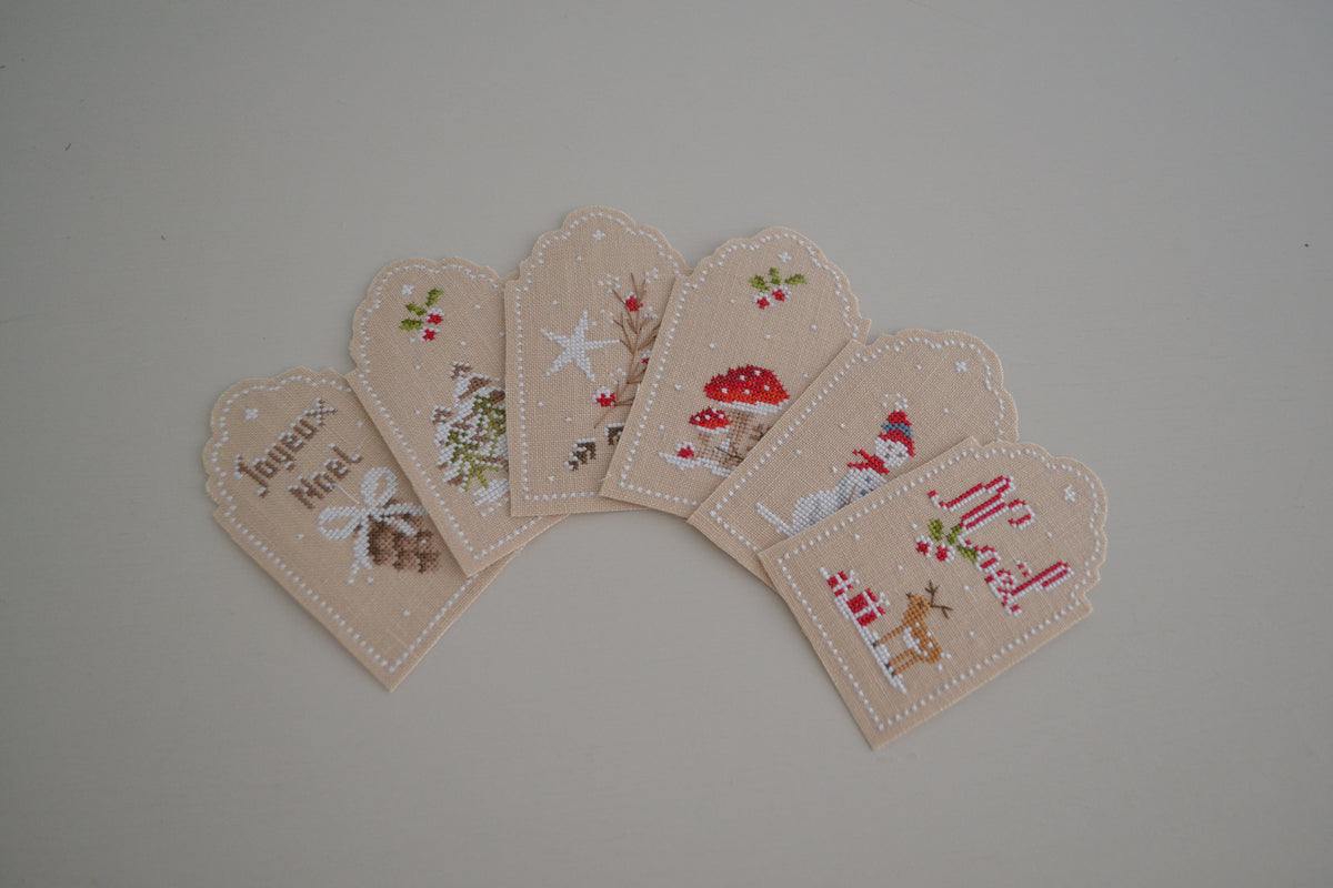 Brodez six étiquettes de Noël au point de croix pour personnaliser vos cadeaux : mots doux et motifs d’hiver. 41 × 70 points sur lin Zweigart 16 fils/cm.
